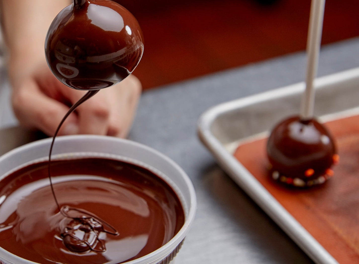 
                  
                    Cake pops in process - chef dunking a cake pop in dark chocolate. A stream of chocolate from the cake pop to the bowl
                  
                