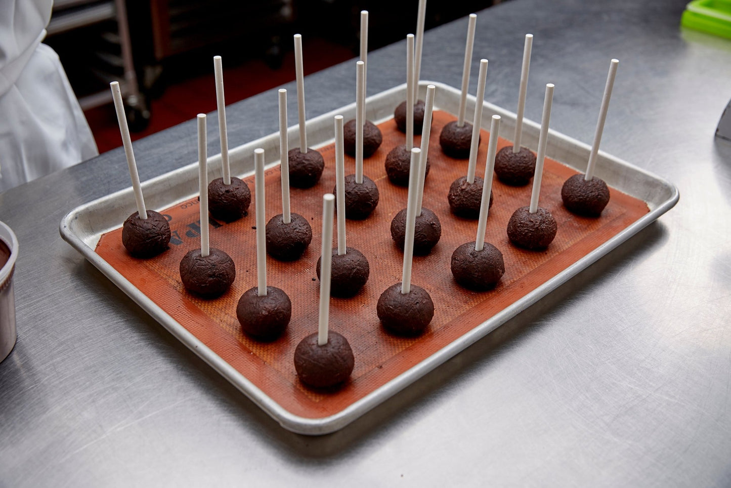 A fresh baked tray of cake pops on a sheet tray getting ready to be dunked into dark chocolate