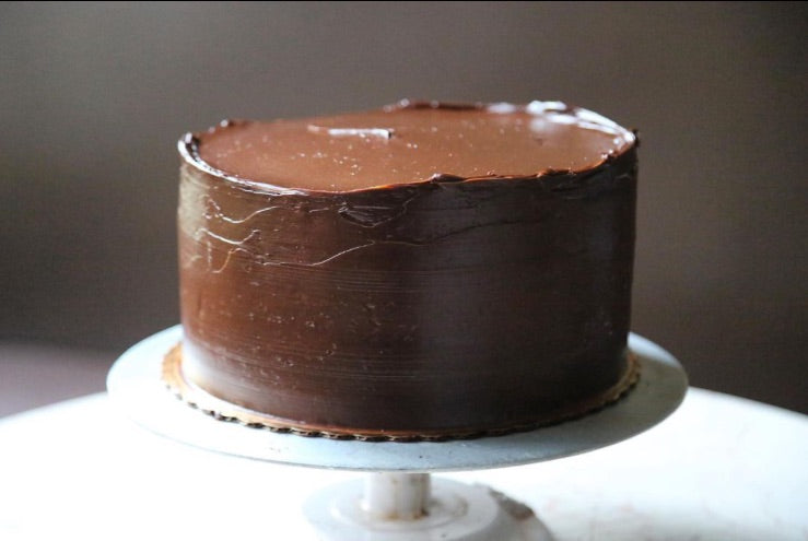 Perfectly frosted chocolate layer cake on a frosting stand on a white marble table