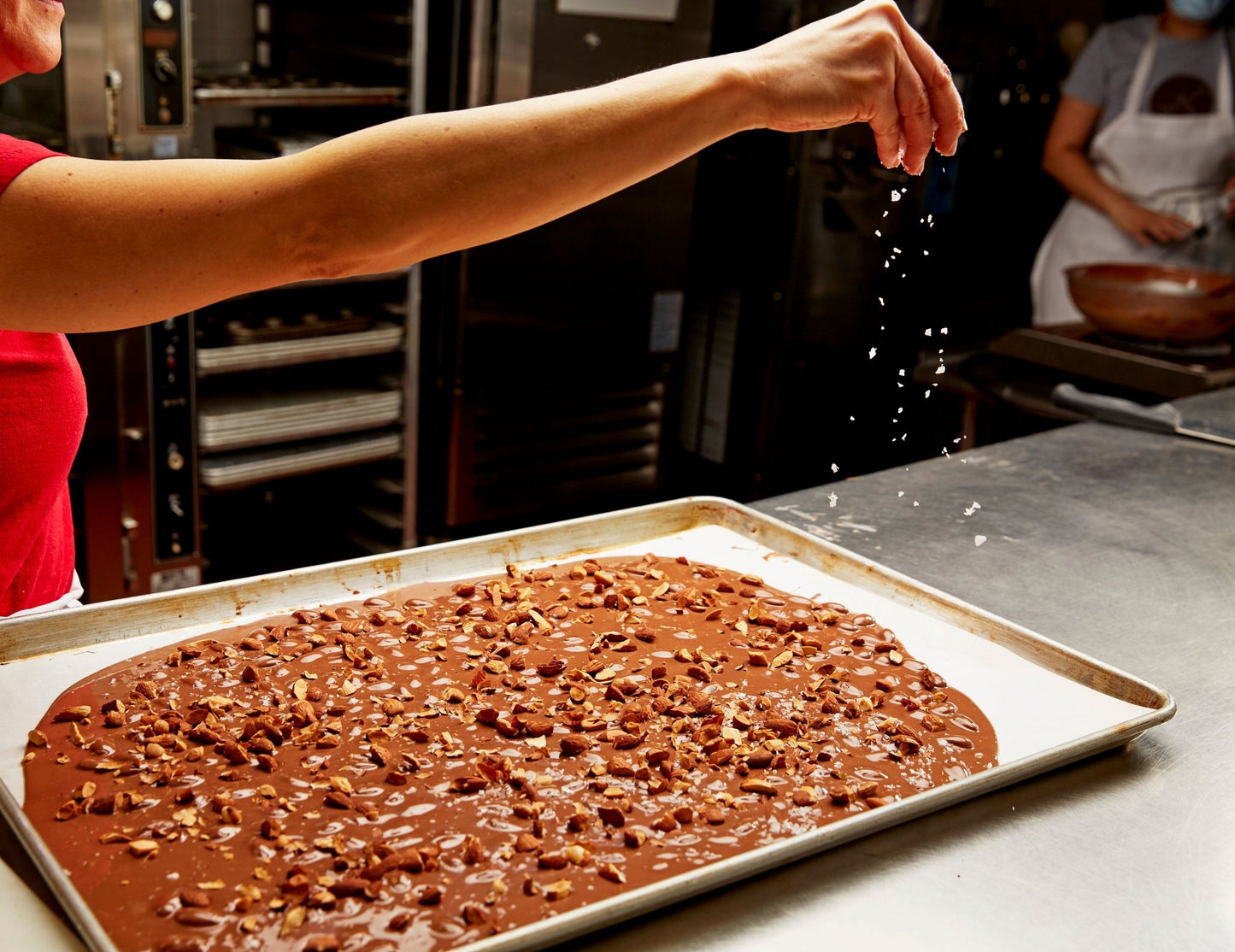 
                  
                    Chef in the kitchen sprinkling sea salt on freshly made milk chocolate bar
                  
                