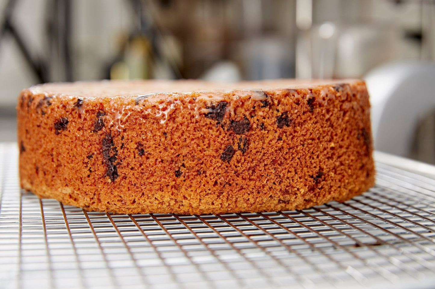 Close up of a chocolate almond cake on a sheet tray with a cooling rack. Cake is without the chocolate glaze