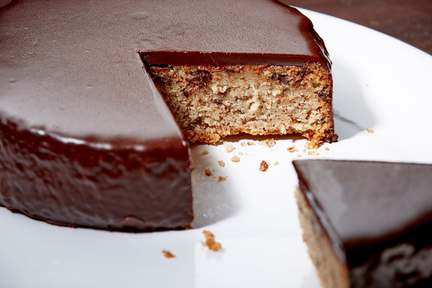 Close up of a chocolate almond cake with one slice pulled out and crumbs on the bright white plate