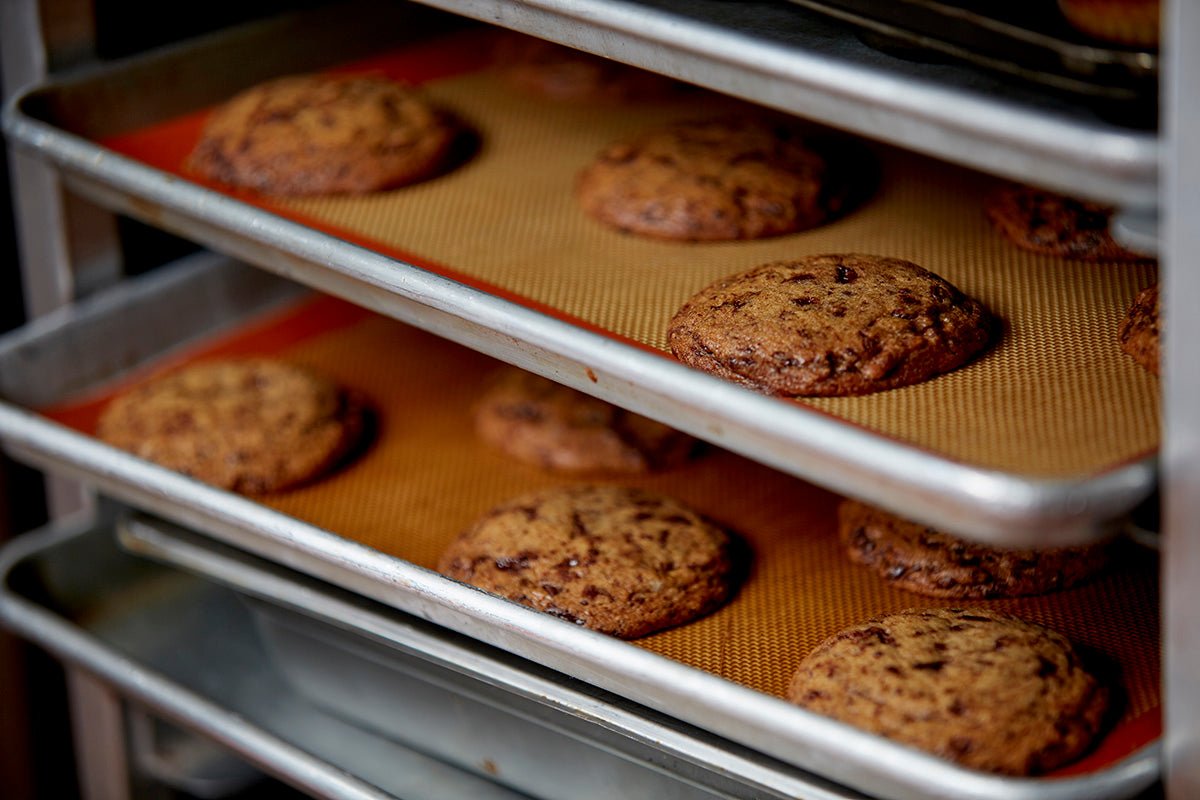 
                  
                    Trays of fresh baked chocolate chip cookies on a speedrack. The cookies are loaded with chocolate chips and have crisp edges
                  
                