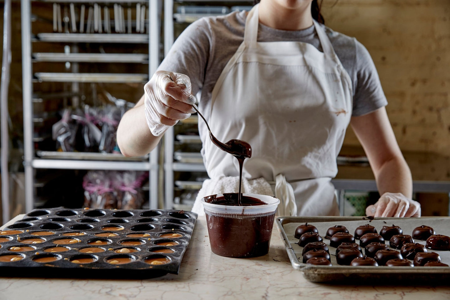 
                  
                    A kitchen scene of a chef dipping s'mores into dark chocolate. Speed racks in the background full of chocolate bunnies
                  
                