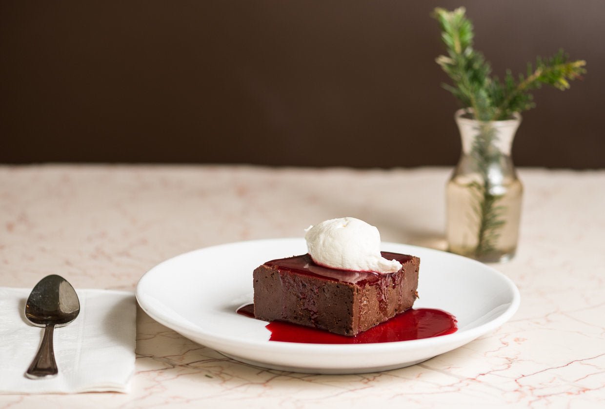 A marble table with a plate of Rich and delicious flourless chocolate cake with raspberry sauce. A spoon on a napkin next it