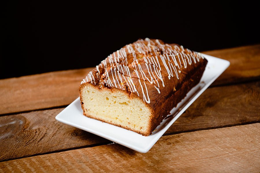 A moody shot of a White Chocolate Pound Cake with drizzled white chocolate zig zagged across the top on a white plate - yum!