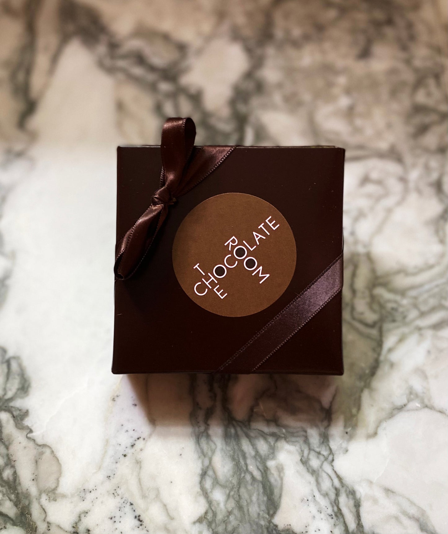 Overhead shot of a custom 4pc bonbon party brown favor branded box on marble tabletop 