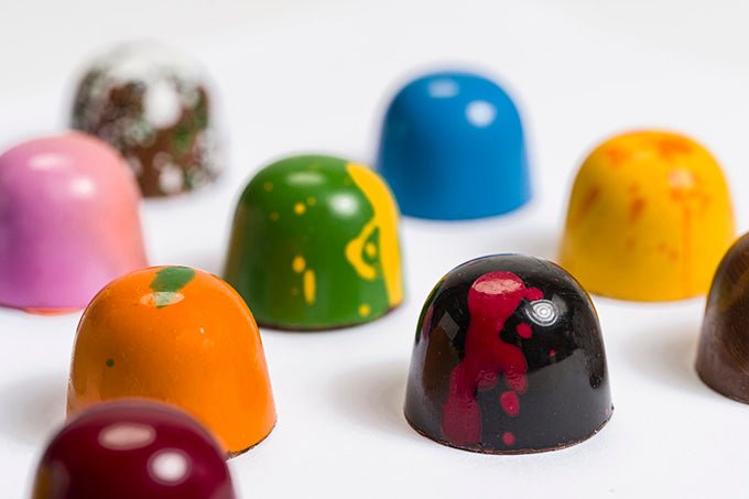
                  
                    Close up view of 12 assorted colorful hand painted bonbons. Some in back have a soft focus
                  
                