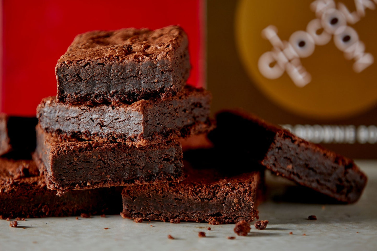 Close up of six stacked mouthwatering brownies in front of a stylish 12 piece brand box of brownies