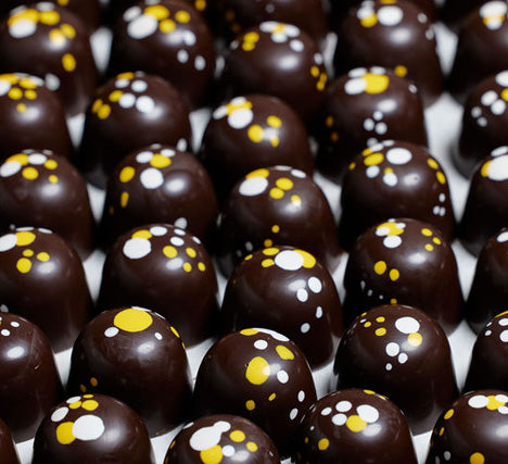 A close up of a tray dark chocolate bonbons with bright yellow and white dots