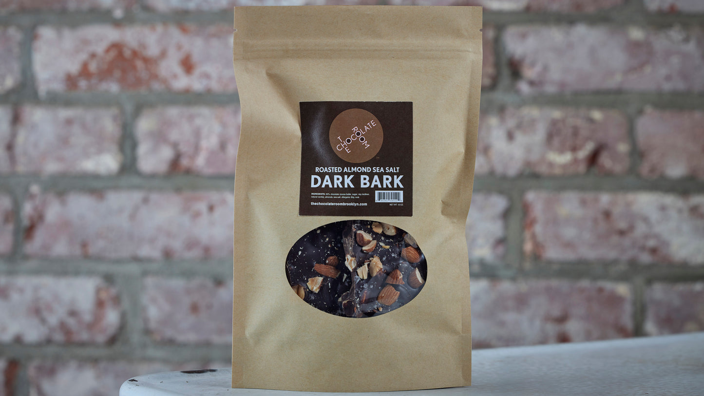Craft pouch of dark chocolate bark, with visible chunks of almonds, sea salt and chocolate through a clear window on front