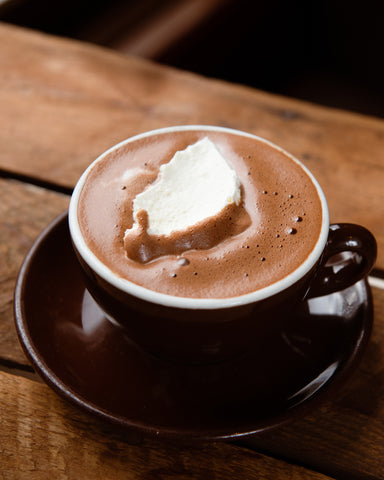A mug of rich hot chocolate with a marshmallow on a wooden crate